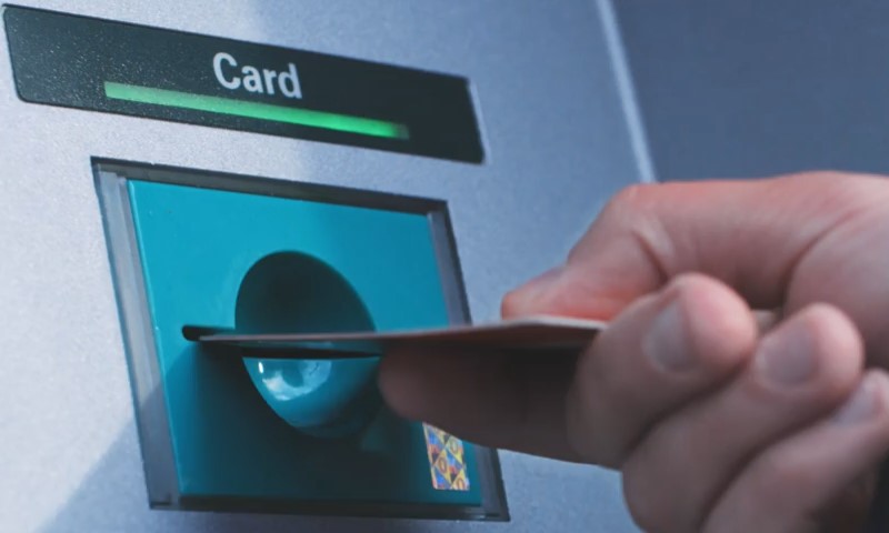 A hand inserts a bank card into an ATM slot