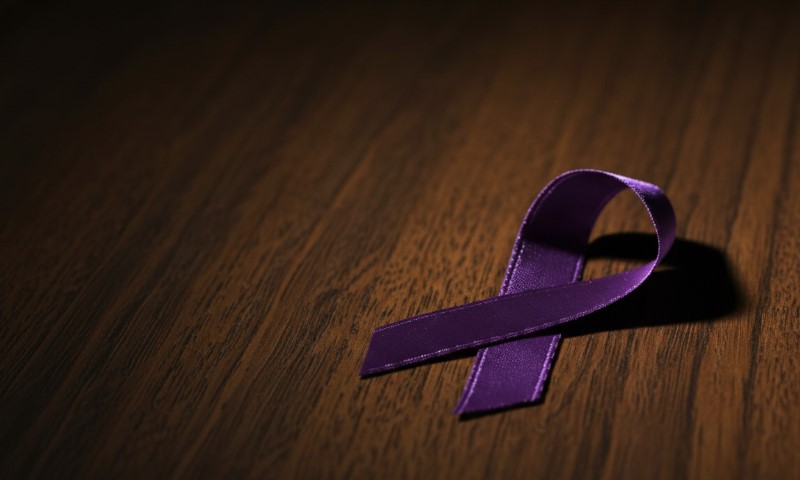 A purple awareness ribbon is placed on a dark wooden surface