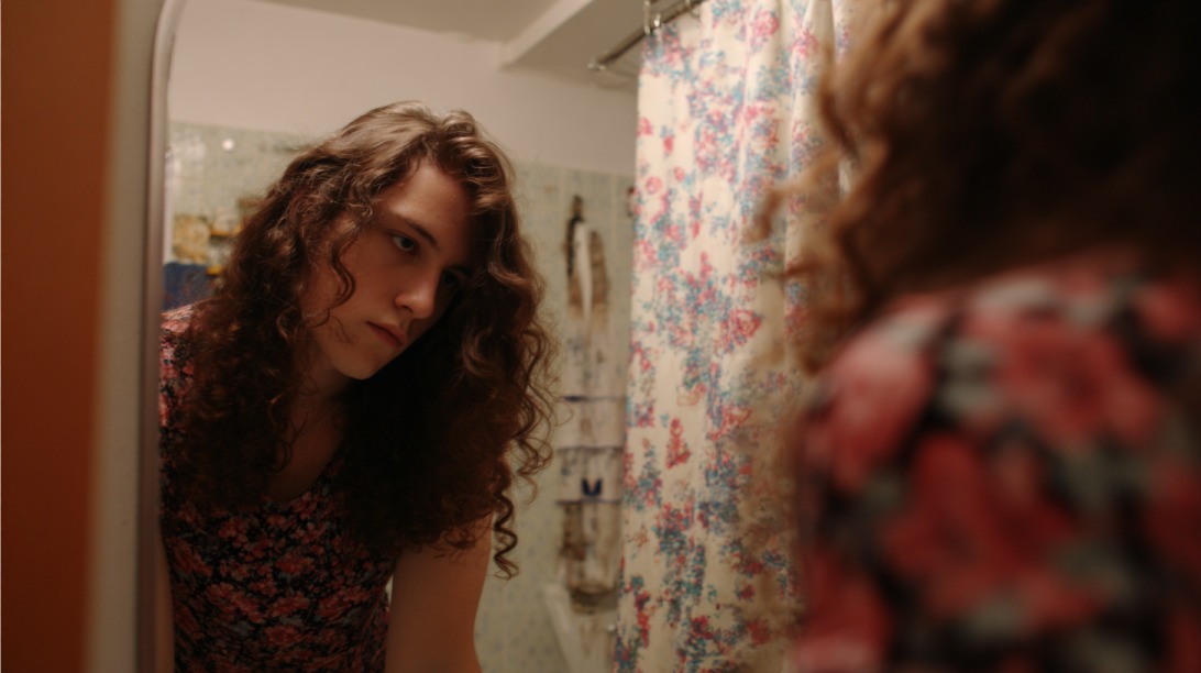 Person with long curly hair looking at their reflection in a bathroom mirror