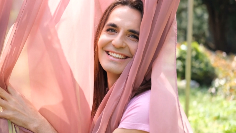 Smiling person outdoors framed by soft fabric