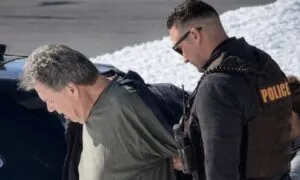 A police officer in tactical gear arrests William Stevenson in a snowy area
