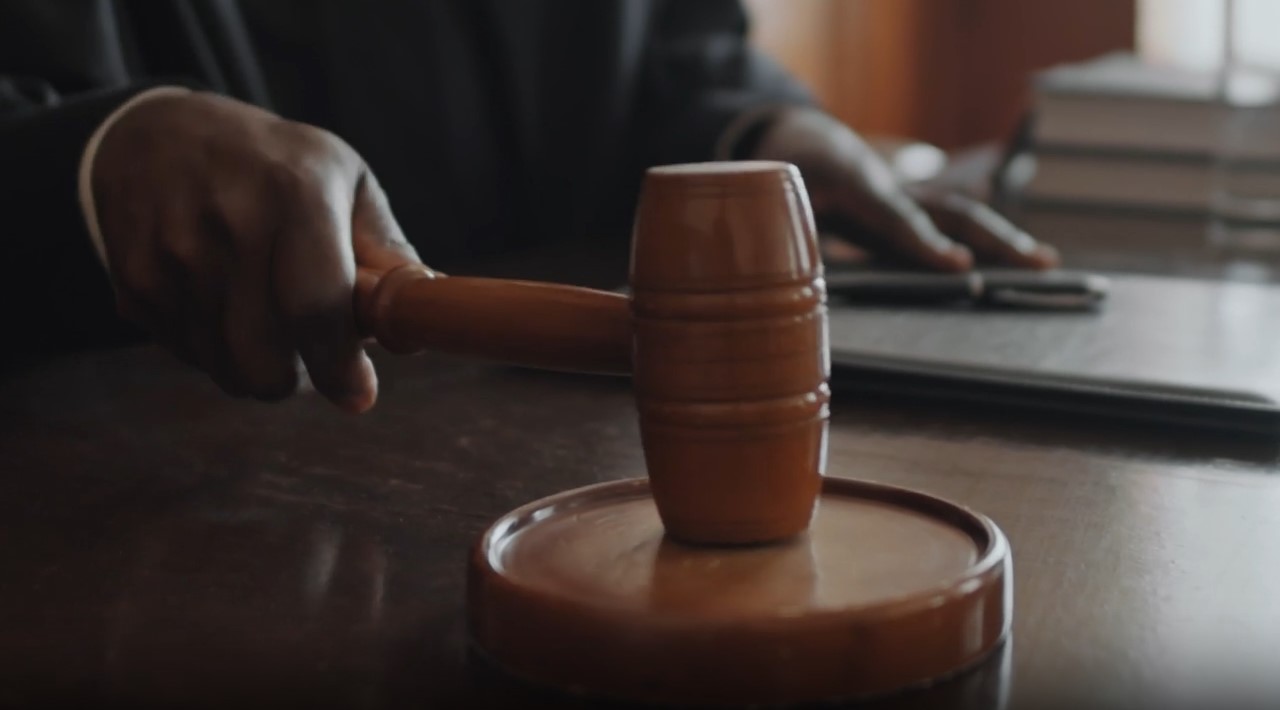 A person holding a wooden gavel poised above a sound block on a judge's desk