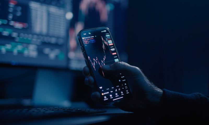 A hand holding a smartphone displaying a stock market chart in a dimly lit room