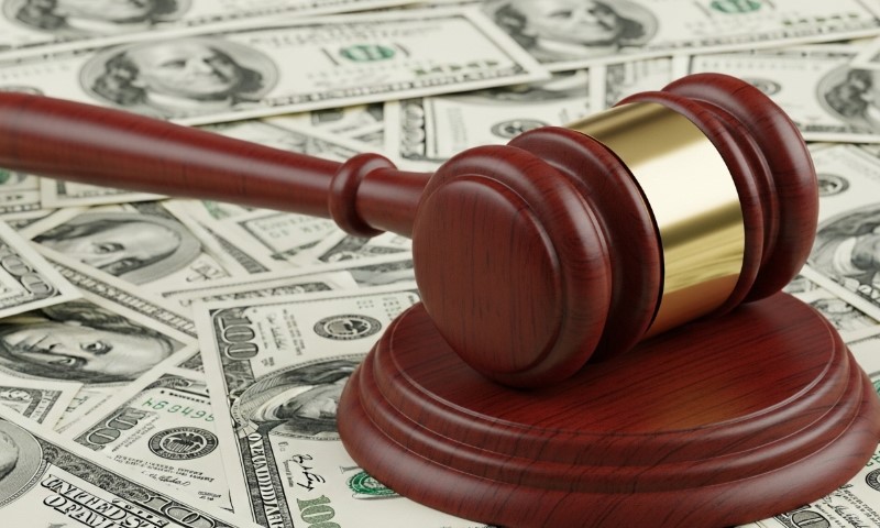 A wooden judge's gavel rests on a base atop a spread of hundred-dollar bills
