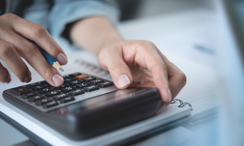 Close-up of hands using a calculator on a notepad. One hand types while the other holds a pencil