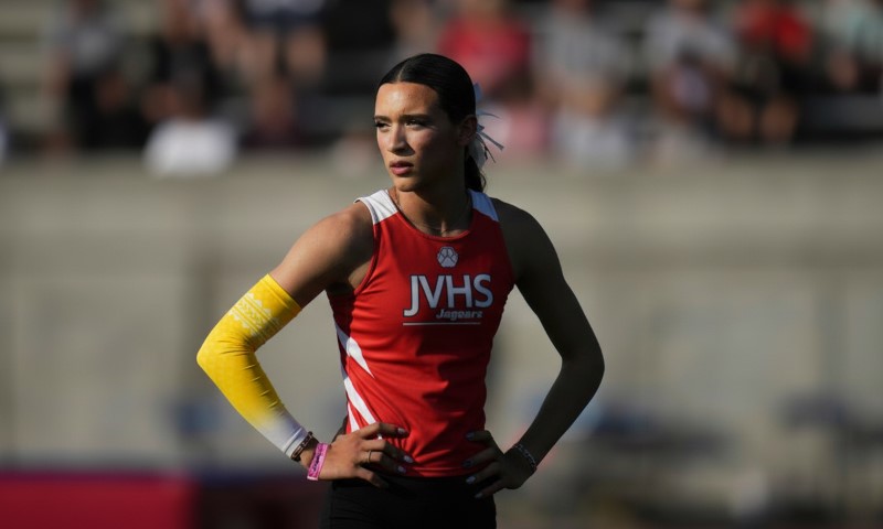 Athlete in a red JVHS jersey and yellow arm sleeve stands on a track field