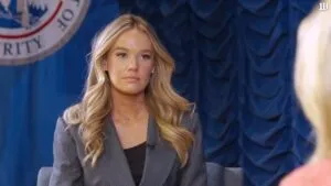 Tricia McLaughlin in a professional interview setting, seated before a dark blue, textured backdrop featuring a partially visible official seal