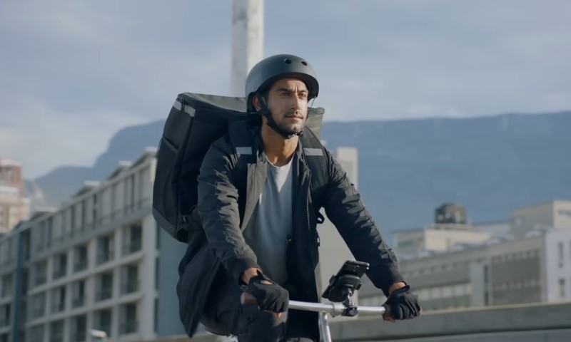 A focused cyclist wearing a helmet and gloves rides with a large backpack in a cityscape