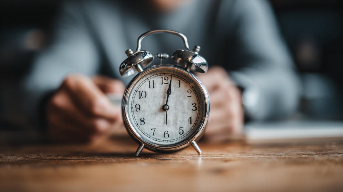Vintage alarm clock on a wooden table with a person blurred in the background