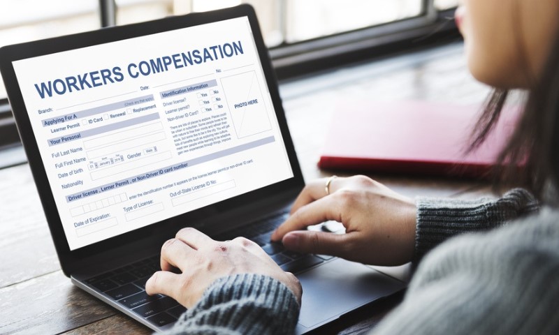 A person types on a laptop showing a "Workers Compensation" form