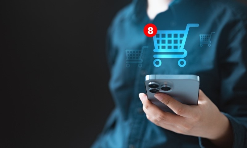 A person holds a smartphone with a digital shopping cart icon and a red notification bubble showing eight