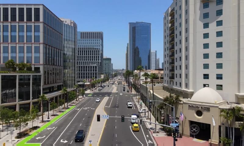 Aerial view of a San Diego street lined with tall, glass buildings and palm trees under a clear blue sky