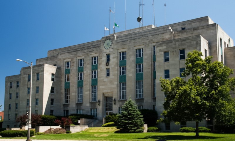 A grand, stone government building with a clock tower, tall windows, and entrance stairs