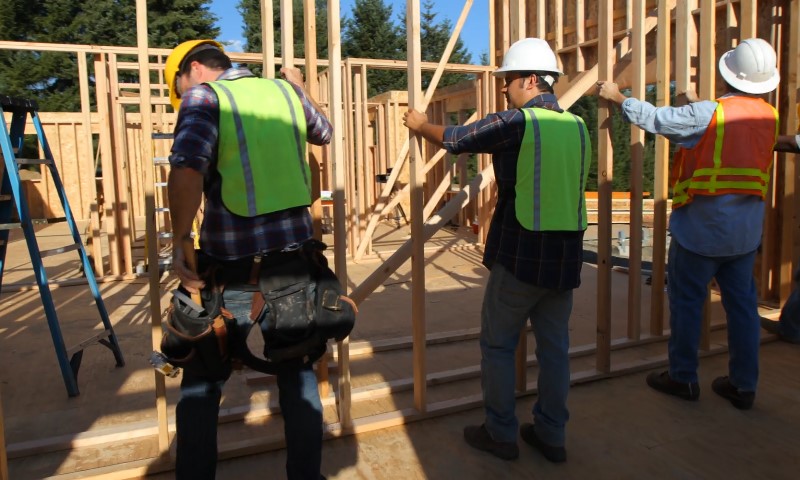 Construction workers in reflective vests and hard hats assemble wooden frames at a building site