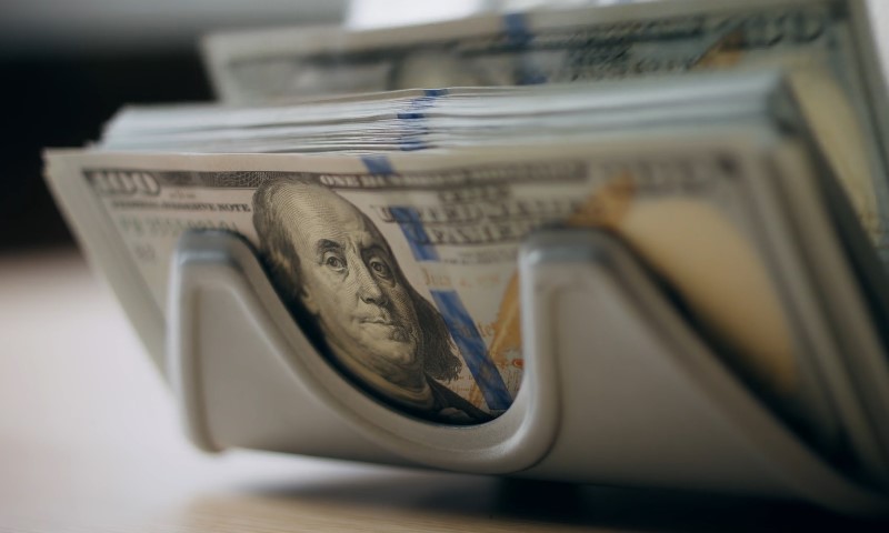 Stack of hundred-dollar bills held by a money counting machine, with Benjamin Franklin's face visible