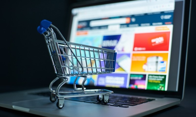 A small shopping cart sits on a laptop keyboard with an online store webpage open in the background