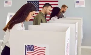 Four people stand at voting booths, casting ballots in a room with American flags