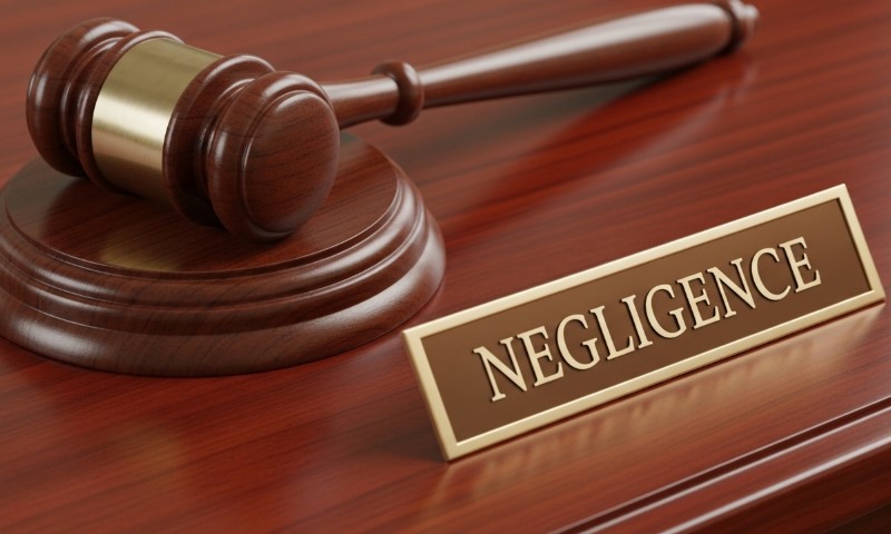 A wooden gavel rests beside a small sign with "Negligence" in bold letters on a polished wooden surface