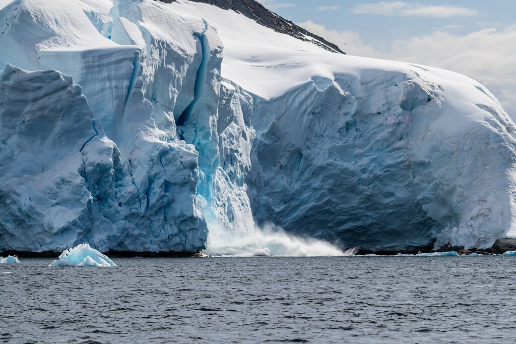 Massive glacier calving into the ocean in Antarctica with visible ice fracture and falling ice blocks