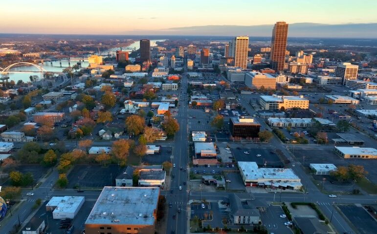 Aerial view of a Little Rock at sunset, featuring a skyline of tall buildings, a winding river, and a bridge