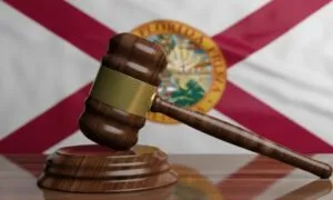 A wooden gavel rests on a sound block in the foreground, set against the Florida state flag