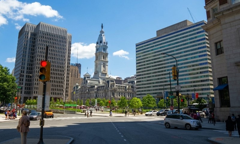 A busy Philadelphia city intersection in daylight, featuring a historic building with a clock tower