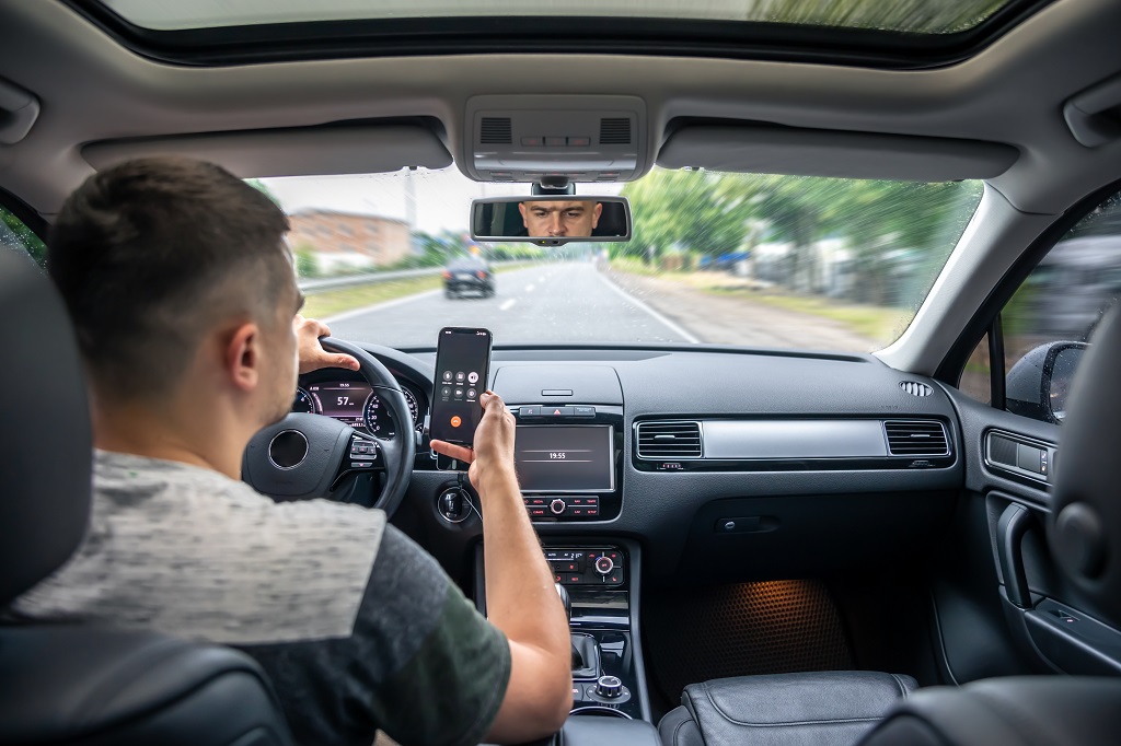 Young driver using smartphone behind the wheel, distracted driving risk