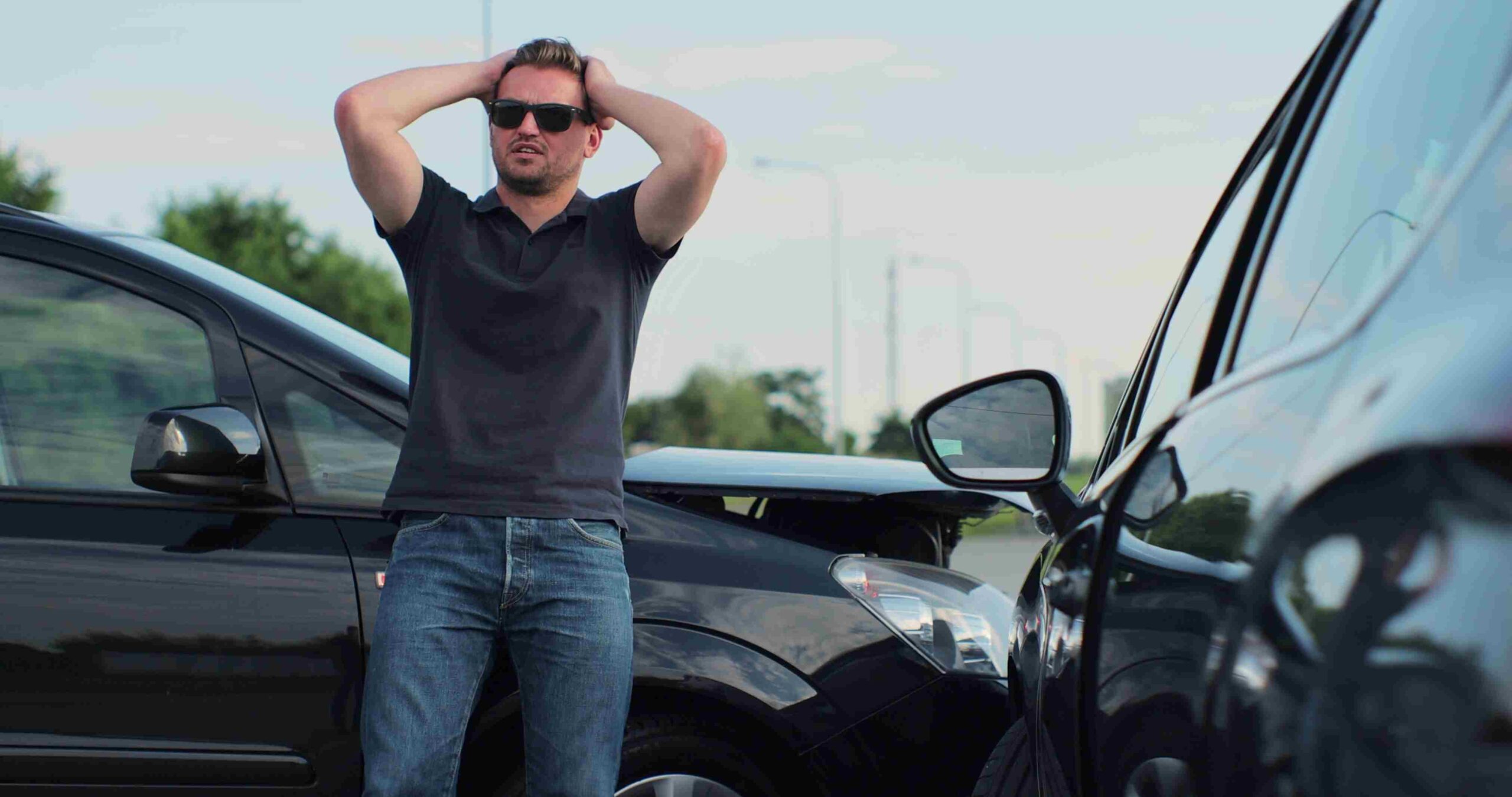 Man holding his head while standing between two damaged cars on the road