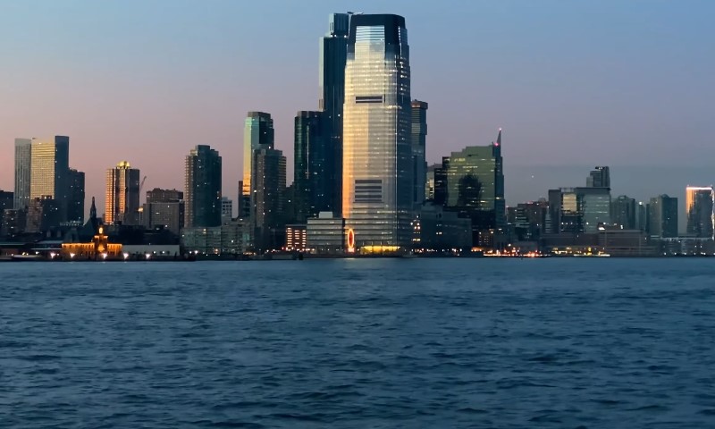 A city skyline at dusk, featuring tall skyscrapers reflecting a soft orange glow