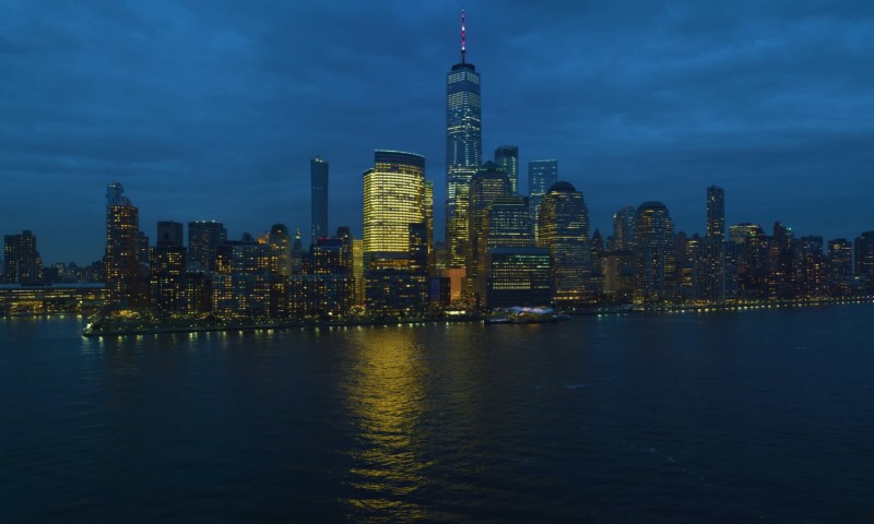 Nighttime view of a city skyline with tall skyscrapers reflecting on the water