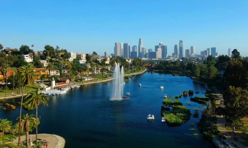 A serene lake in Orange County, with a central fountain is surrounded by palm trees, boats, and lush greenery