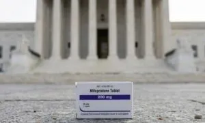 A box of Mifepristone tablets is featured prominently in the foreground, placed on stone steps