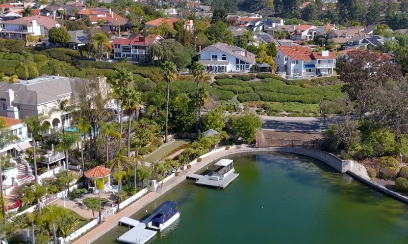 Aerial view of a serene lakeside neighborhood in Mission Viejo with lush greenery, elegant houses, and private docks