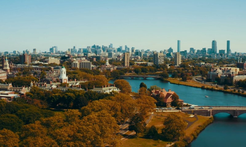 Aerial view of a cityscape with a river winding through, surrounded by autumn-colored trees