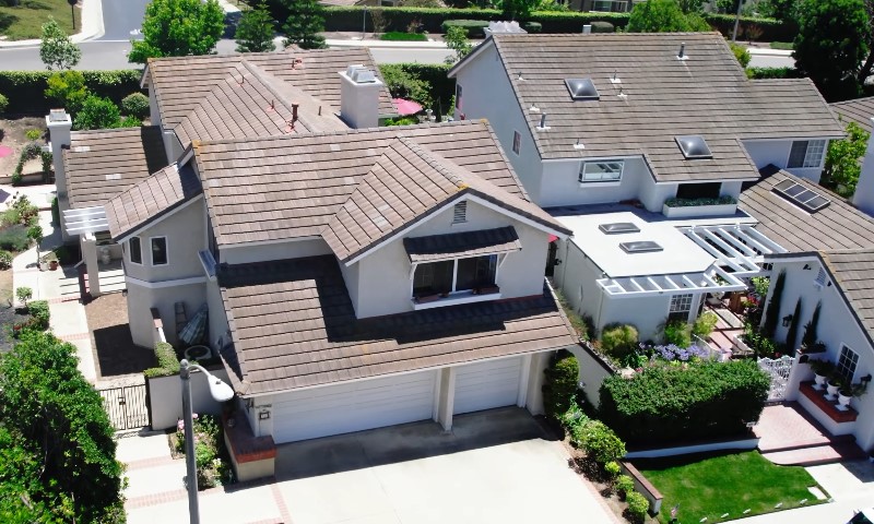 Aerial view of suburban houses with brown tiled roofs, white exteriors, and neatly landscaped gardens