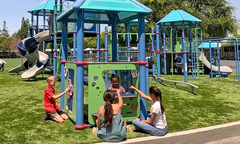 Children play on a colorful playground with slides and climbing structures, enjoying a sunny day
