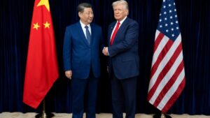 Xi and Trump shake hands in a formal setting, standing between the flags of China and the USA.
