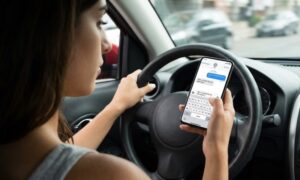 A woman texting on her smartphone while driving, holding the device over the steering wheel