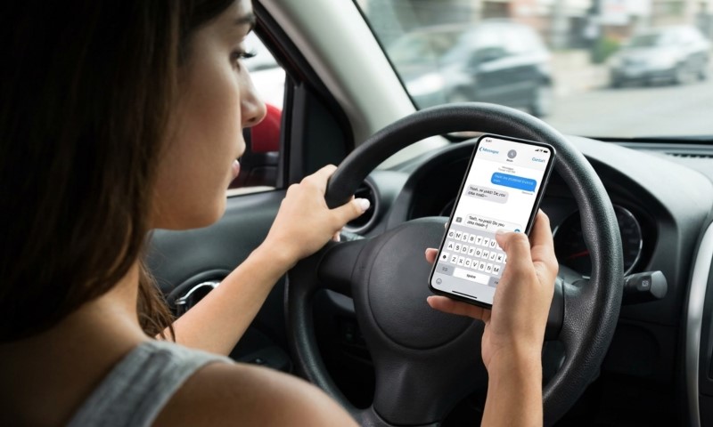 A woman texting on her smartphone while driving, holding the device over the steering wheel