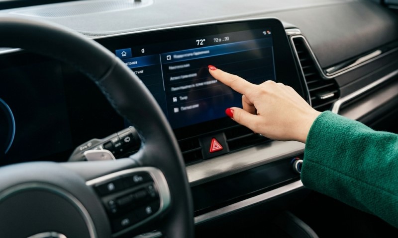 A person with red nail polish touches a car's touchscreen dashboard