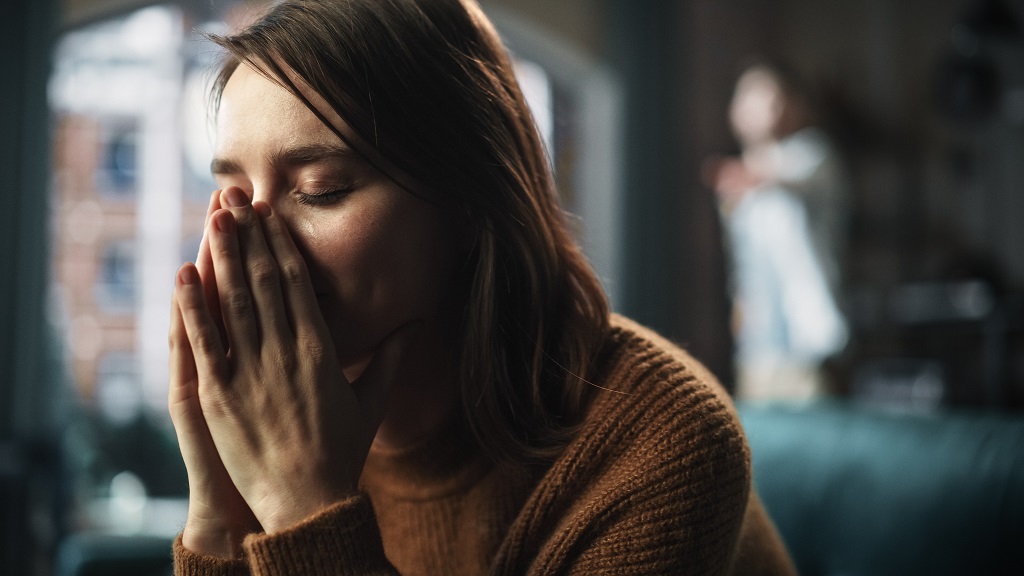 Woman covering her face in distress while another person stands blurred in the background
