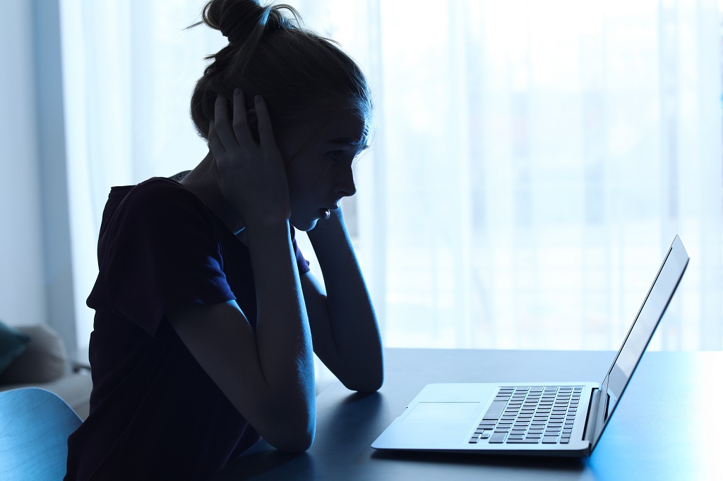 Distressed young person sitting alone at a laptop while facing online abuse and emotional pressure