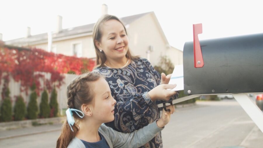 A woman and child place election mail into a residential mailbox