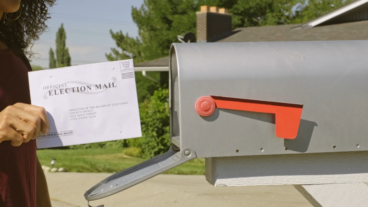 A voter holds an official election mail ballot beside a residential mailbox