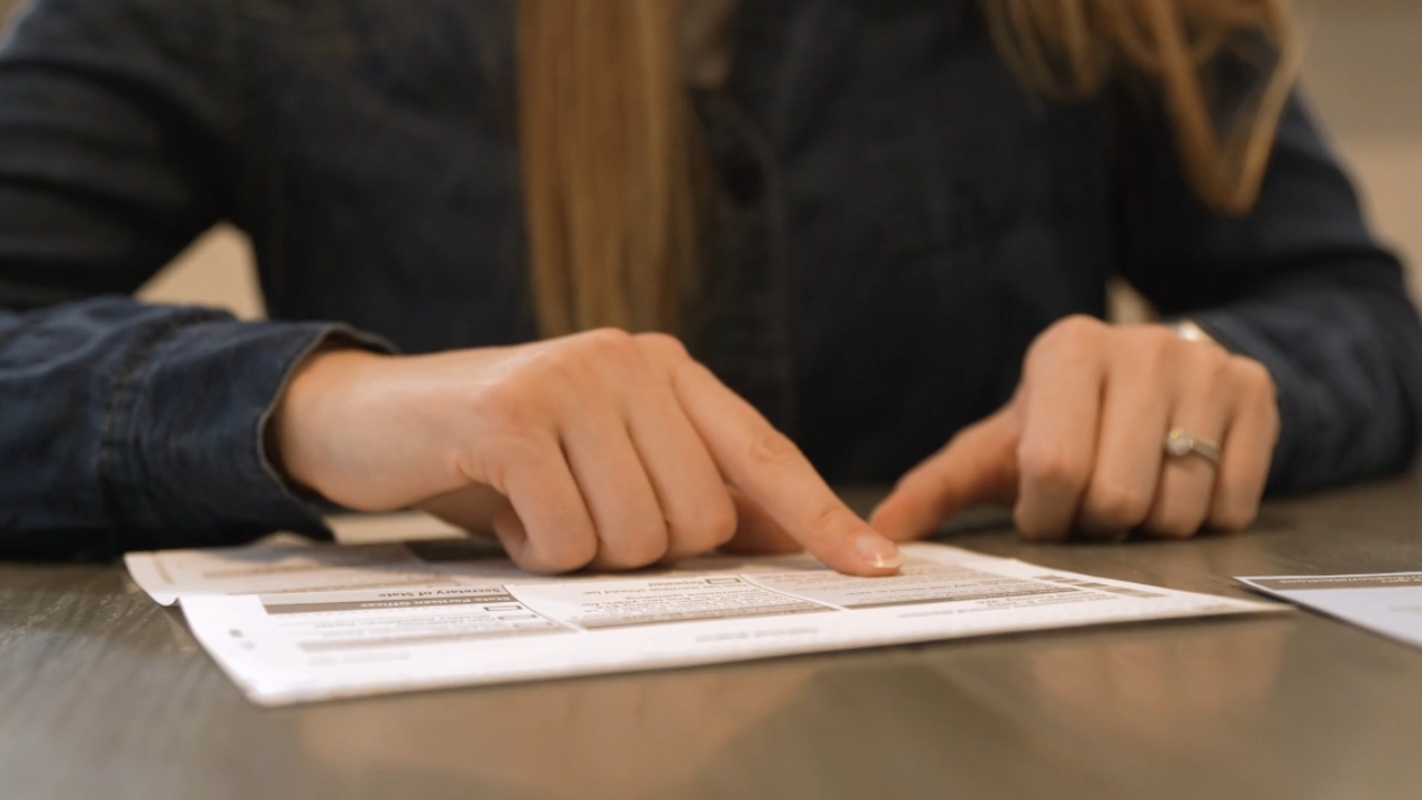 A voter points to a mail ballot form on a table