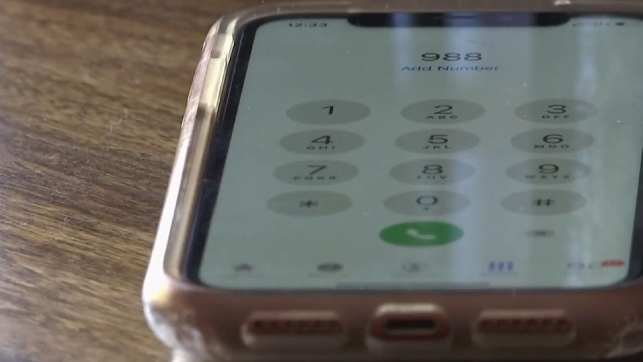 A smartphone displays 988 on the dial pad for the Suicide & Crisis Lifeline.