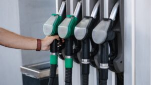 A hand selects a fuel pump nozzle at a gas station.