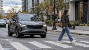 Pedestrian steps off a sidewalk beside the front bumper of a gray SUV on a city street.