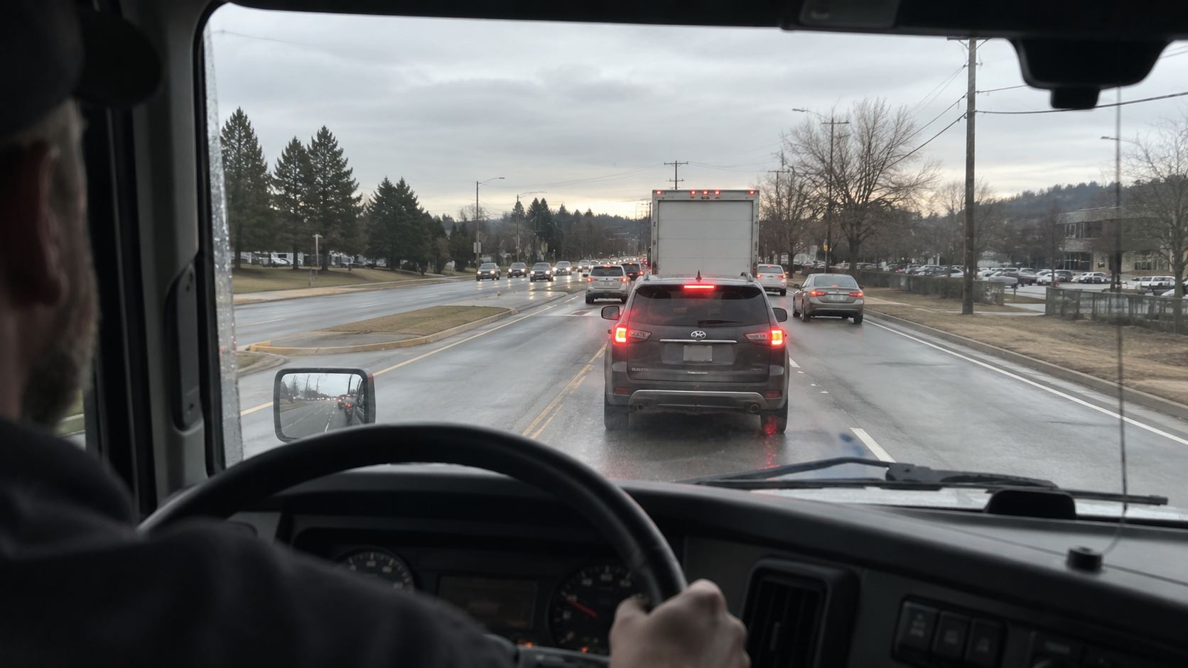 View from a truck cab toward vehicles braking on a wet road.