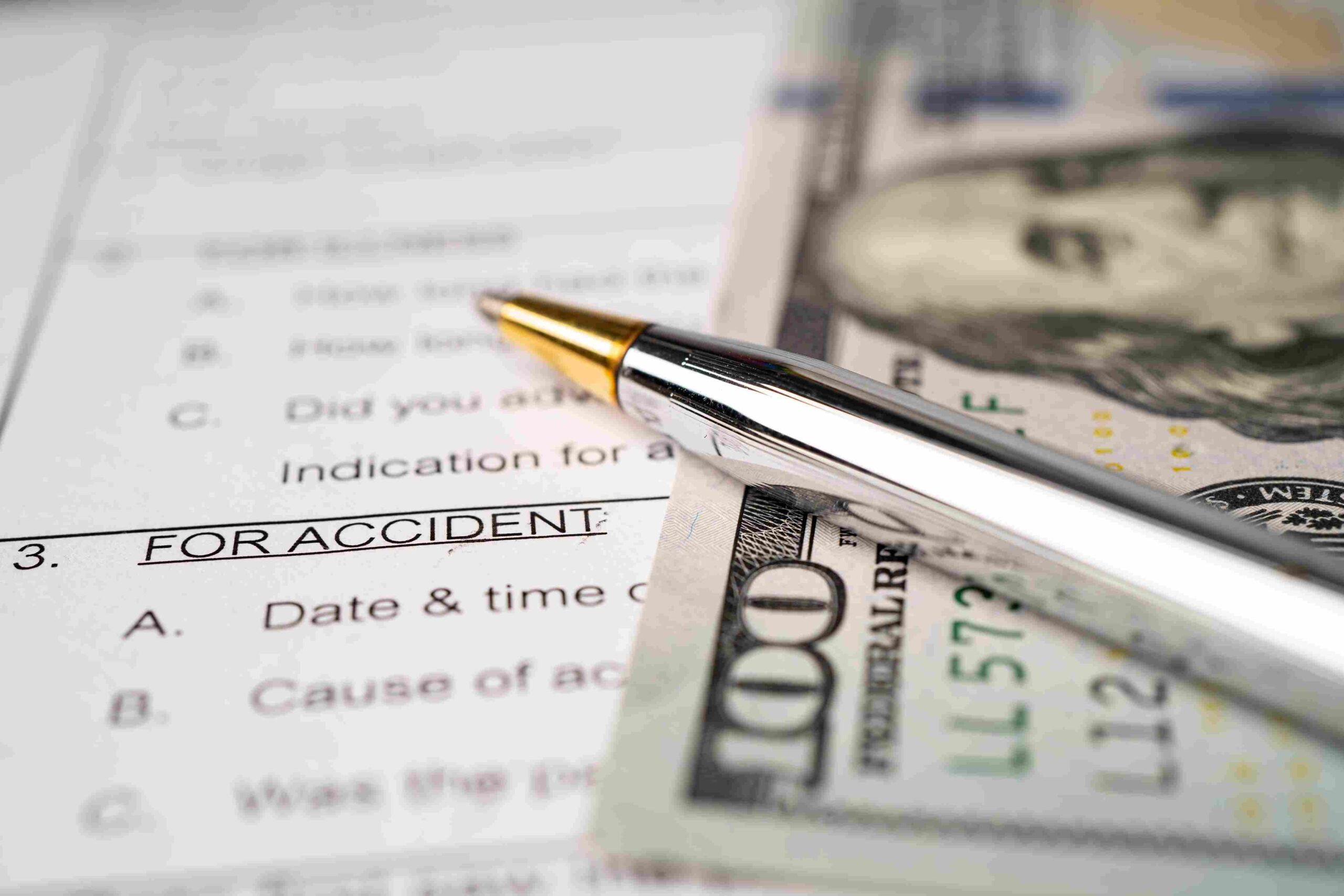 -up of an accident claim form, a silver pen, and a $100 bill representing an insurance rate dispute.